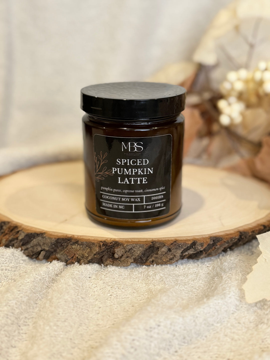 Jar of 'Spiced Pumpkin Latte' candle on a wooden surface with a blurred background