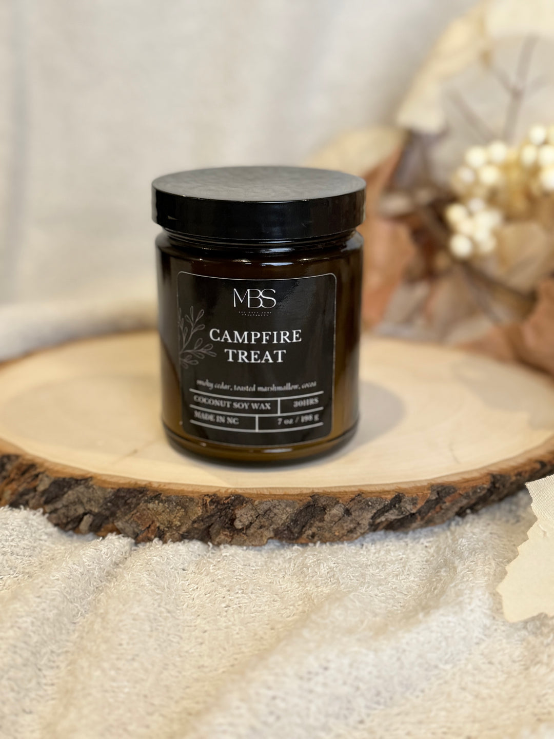 Jar of 'Campfire Treat' candle on a wooden surface with a blurred background