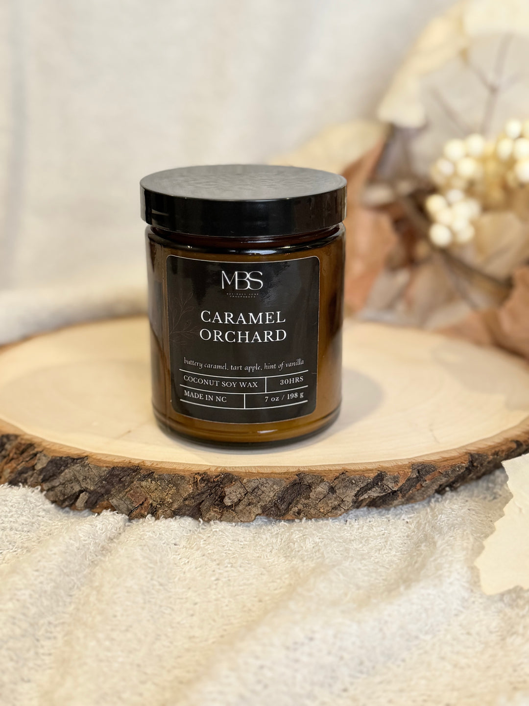 Jar of 'Caramel Orchard' candle on a wooden surface with a blurred background