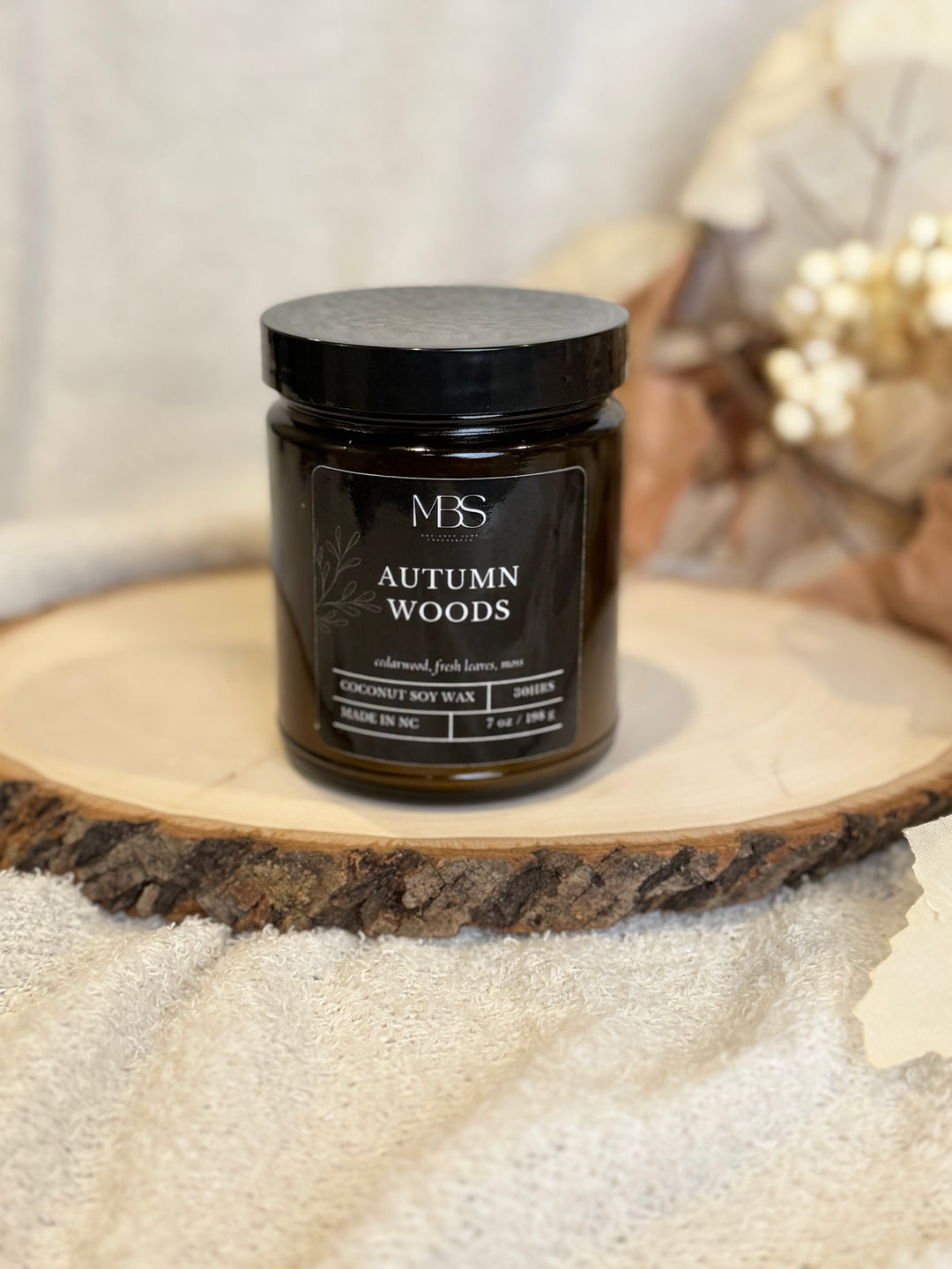 Jar of 'Autumn Woods' candle on a wooden surface with a blurred background